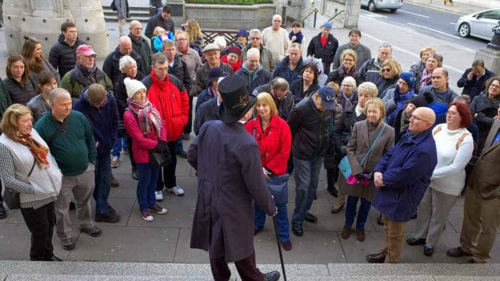 London, England - December 28, 2015: A man in a top hat and coat addresses a crowd of people as part of guided tour in Threadneedle Street, London