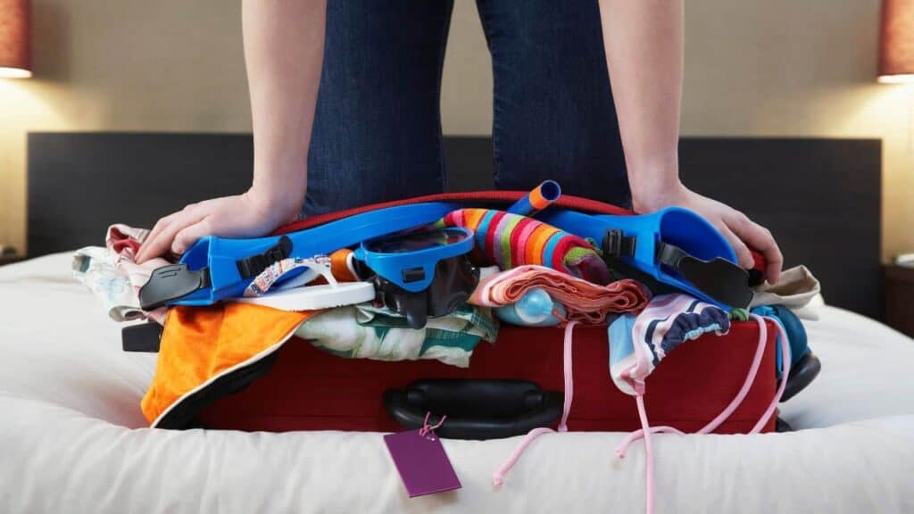 Overstuffed suitcase with someone kneeling on top trying to get it to shut
