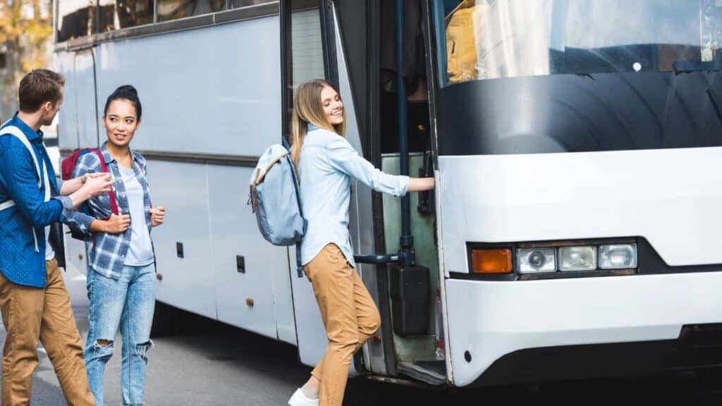 Selective focus of multiethnic tourists with backpacks walking into travel bus at city street