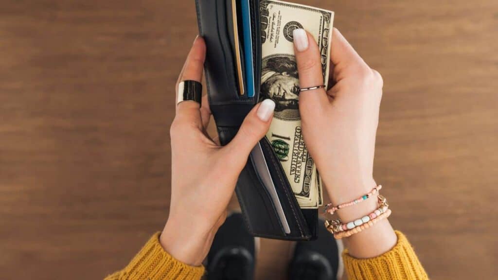 Top view of woman taking from wallet dollars banknotes on wooden background