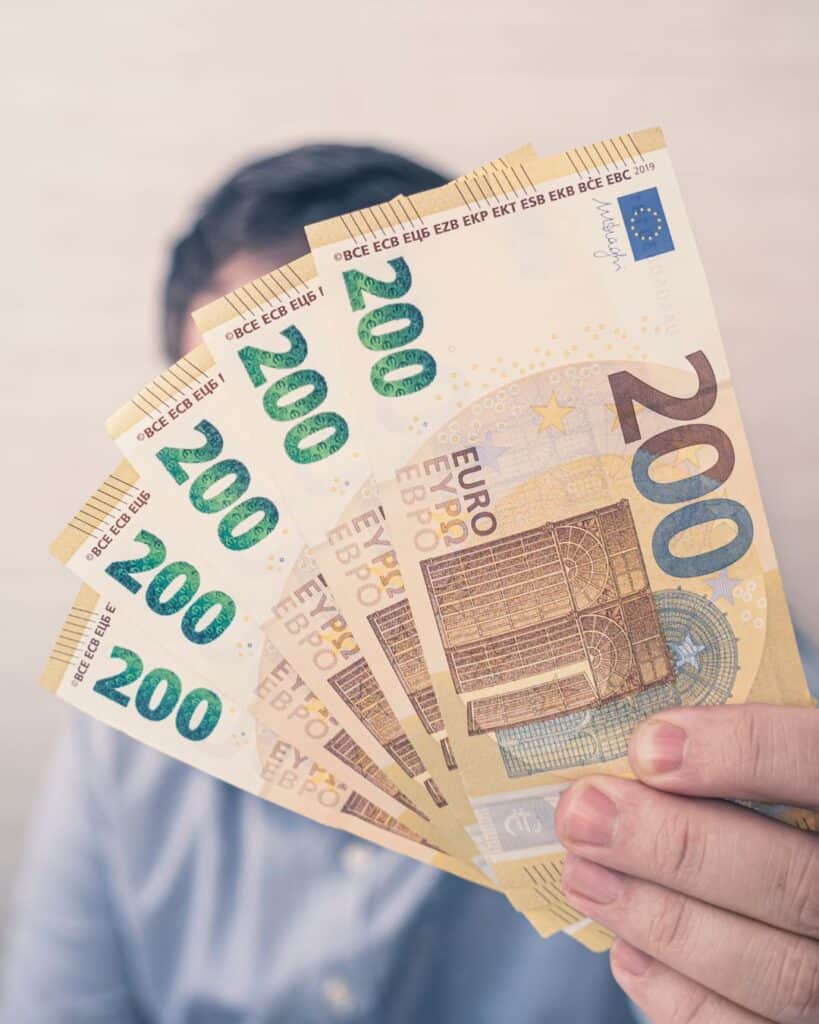 A person holds out a fanned stack of 200 euro notes.