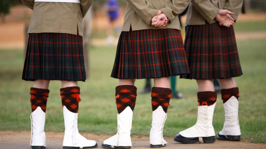 Three men wearing kilts and boots.