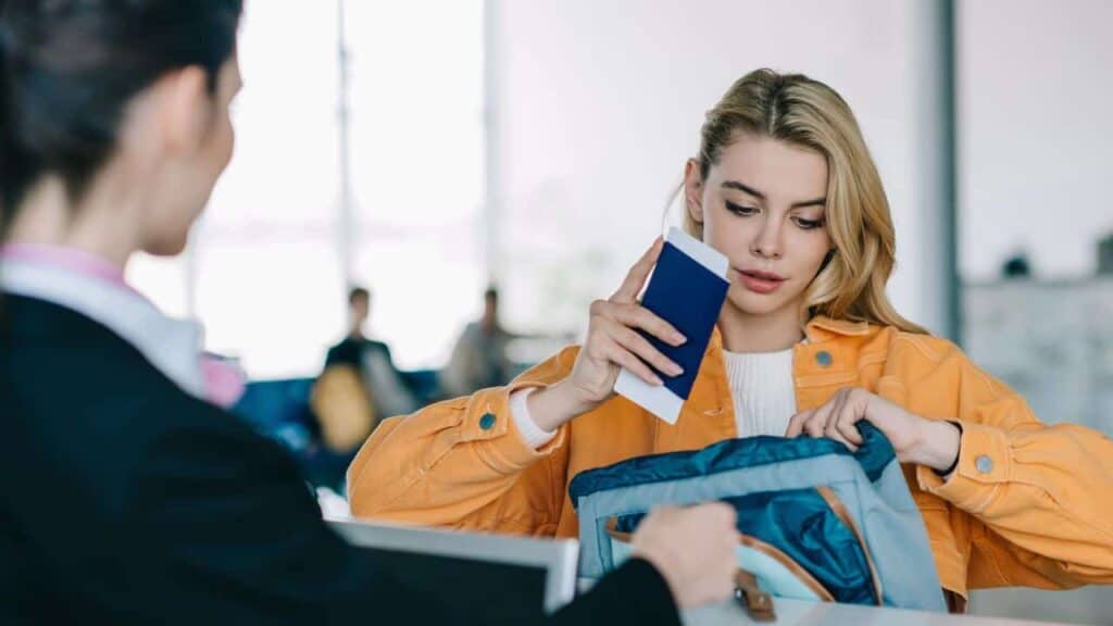 Young woman putting passport with boarding pass into bag at check-in desk in airport