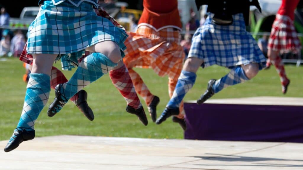 Highland dancers jumping up wearing plaid skirts