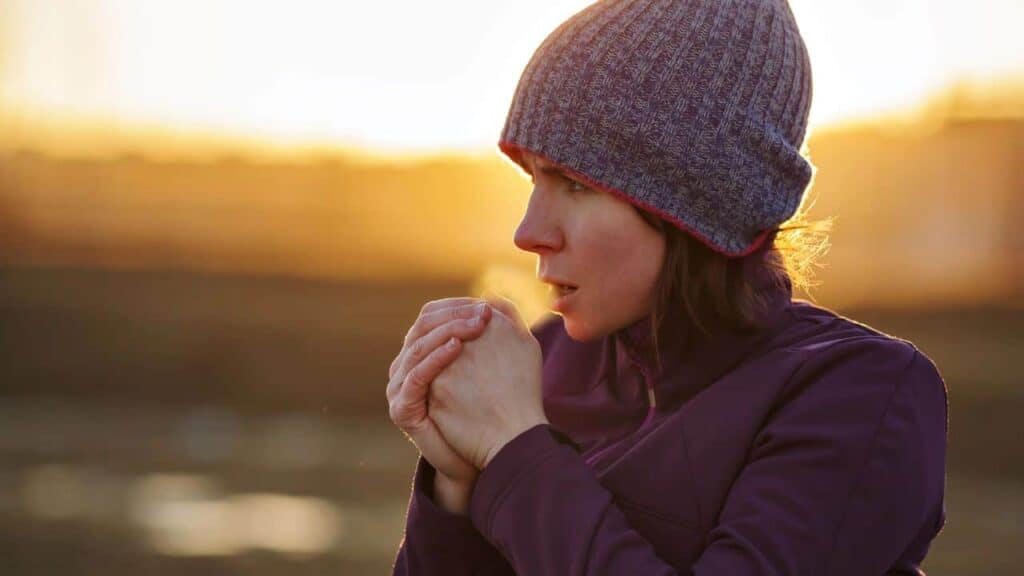 Woman wearing a beanie breathing into her hands to warm them up.